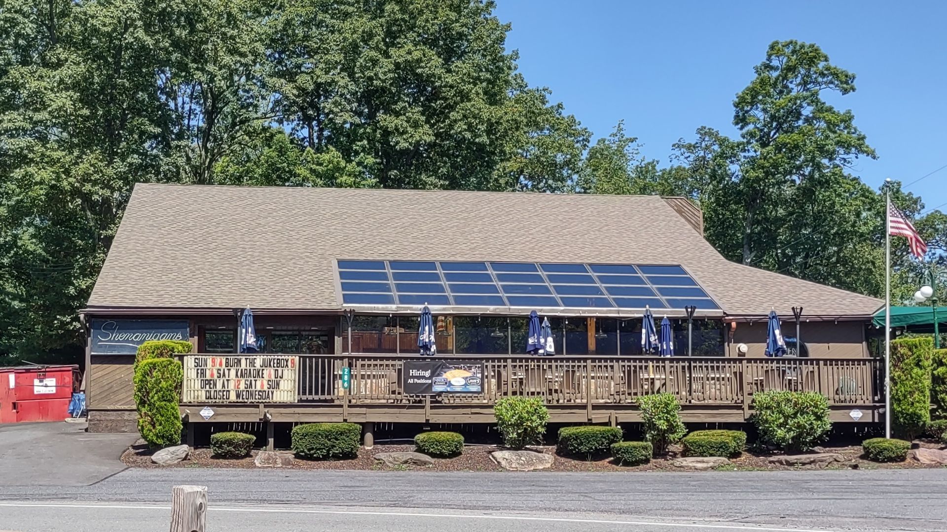 Restaurant with brown siding and roof, outdoor deck, solar panels, and American flag.