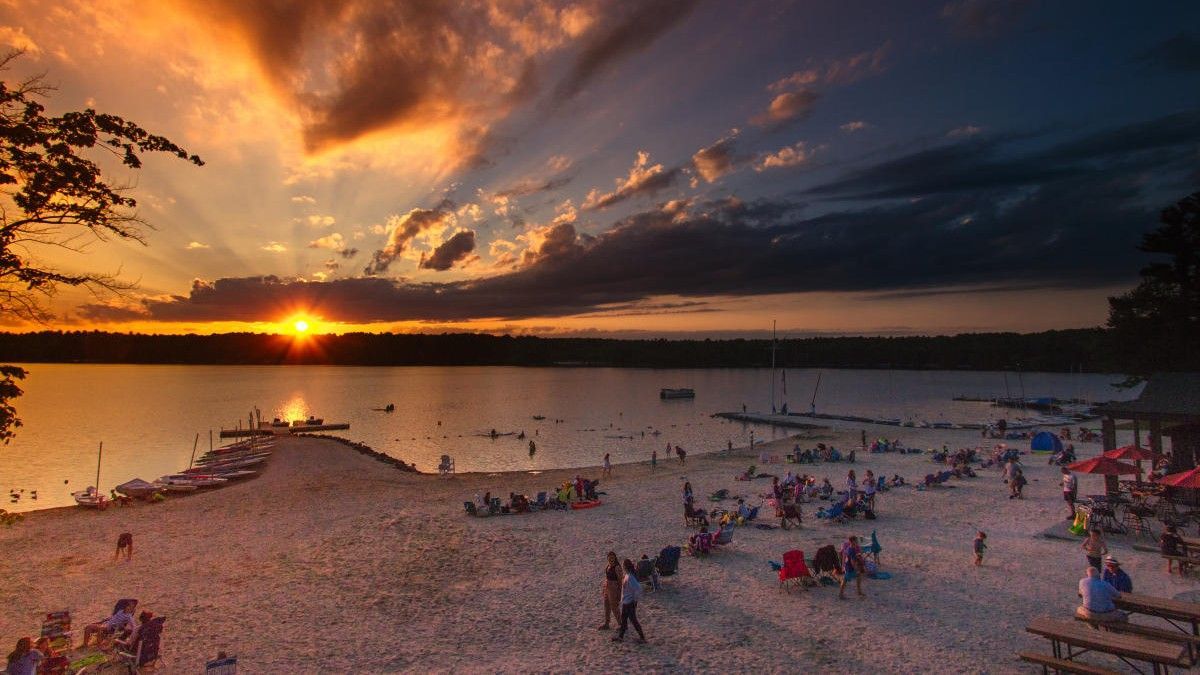 Sunset over a beach with people relaxing, orange sky reflecting on the water.