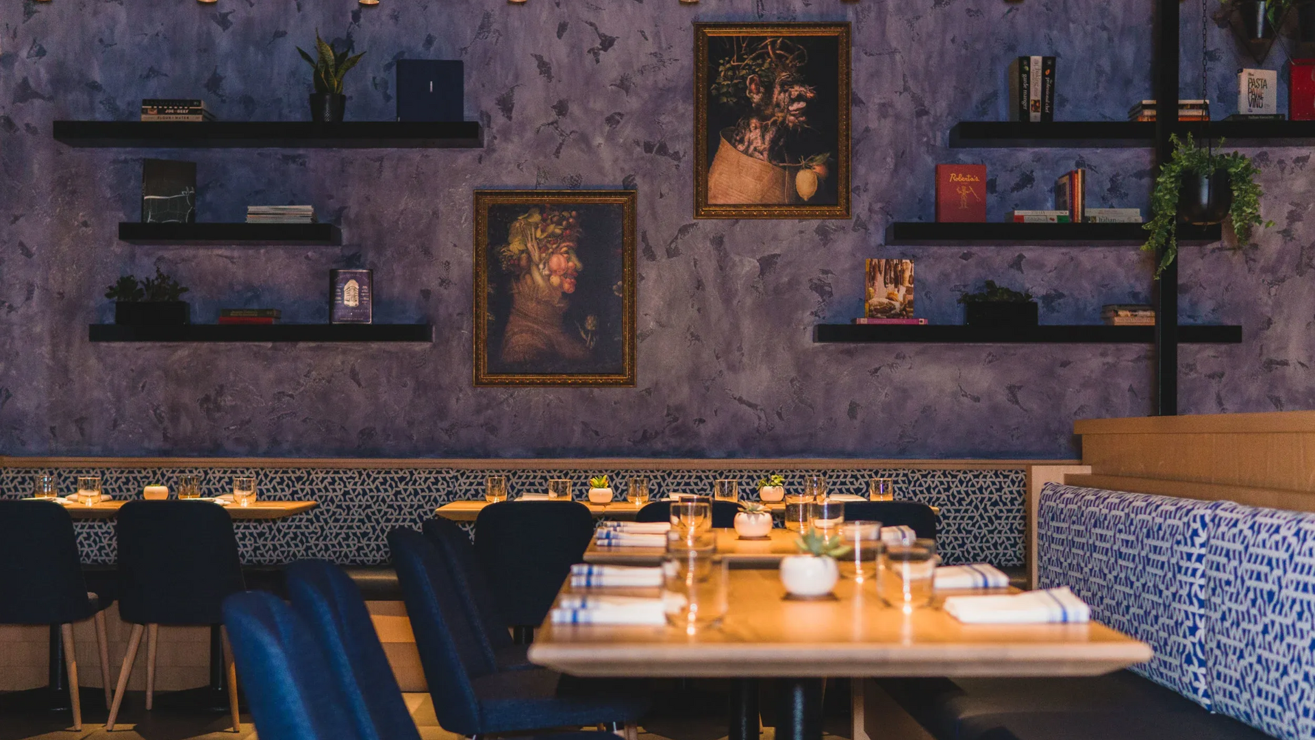 Restaurant interior with tables set for diners, blue chairs and patterned wallpaper, and artwork.