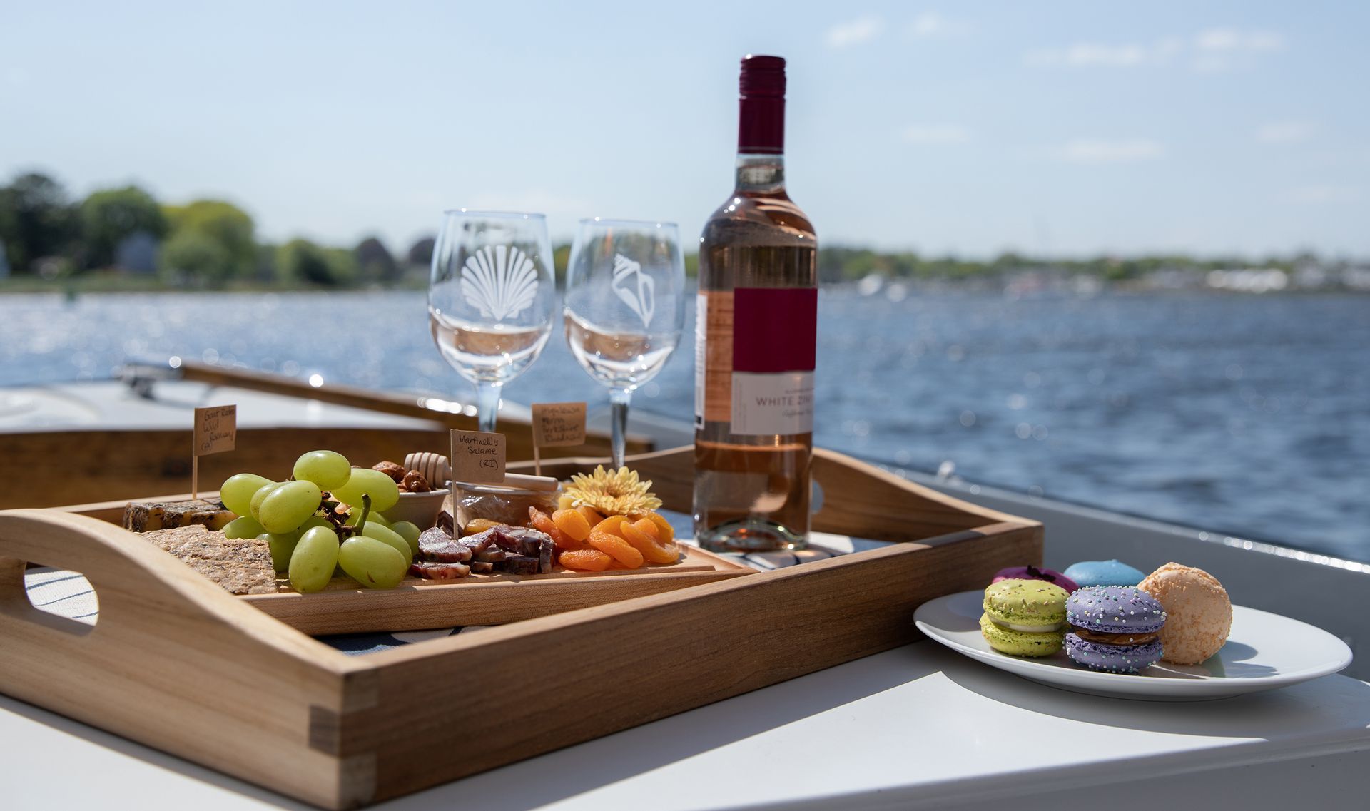 Charcuterie tray with wine and macarons on a boat. The water and blue sky are in the background.