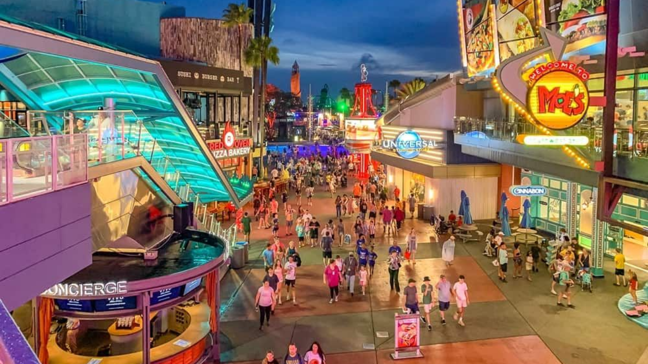 Crowded outdoor pedestrian area at dusk, lit by neon signs. Includes Panda Express restaurant and many people walking.