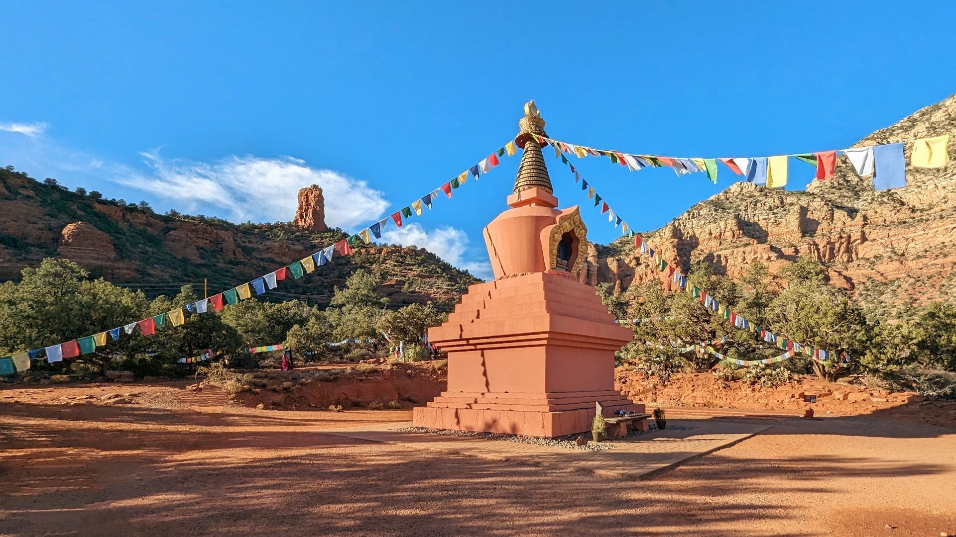 Red stupa with prayer flags against red rock formations and blue sky.