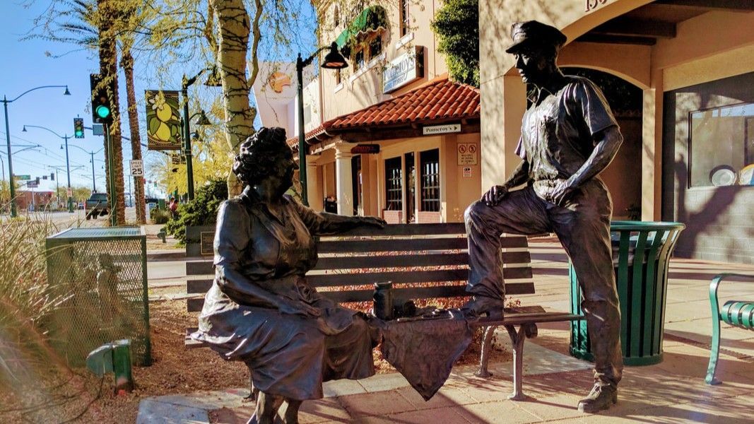 Bronze statues of a woman seated on a bench and a man leaning on the bench, in a town square.