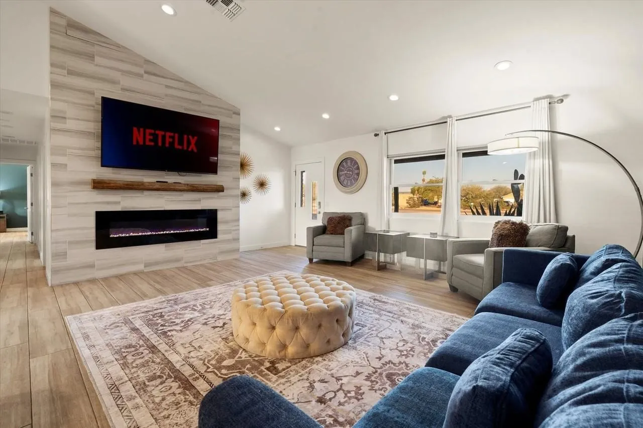 Modern living room with blue sectional, wall-mounted TV, fireplace, and large windows.