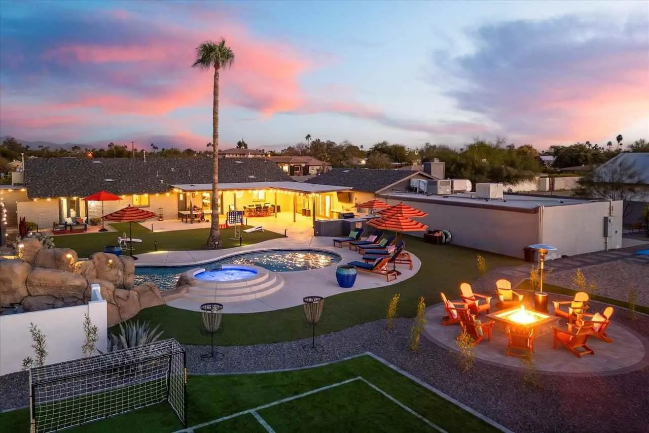 Backyard patio with lit fire pit, pool, palm trees, and pink sunset sky
