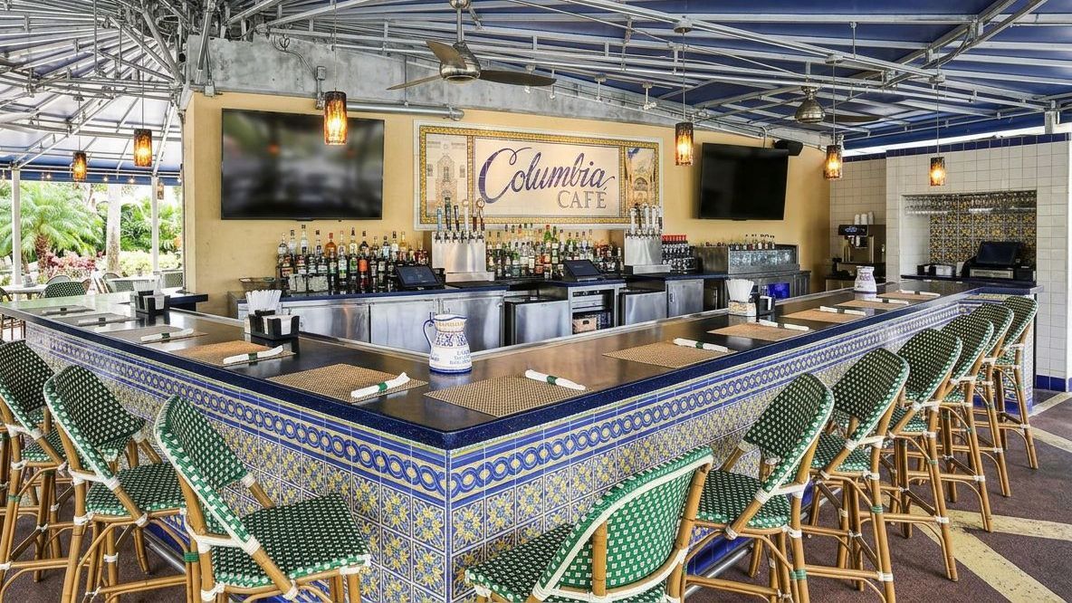 Open-air bar and lounge with blue tiled counter, green chairs, and hanging lights