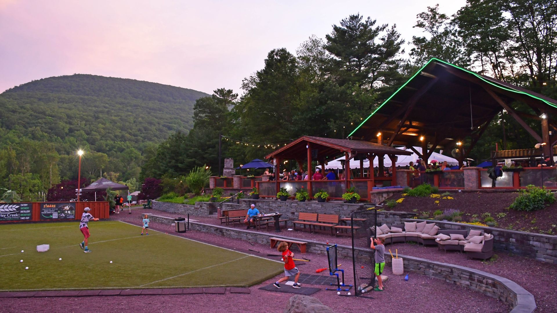 People playing outdoor games at a restaurant with mountain backdrop at dusk.