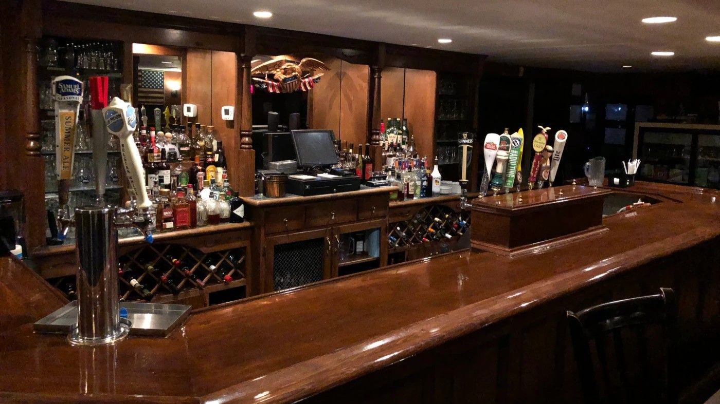 Interior view of a bar with a long wooden counter, liquor bottles, and tap handles.