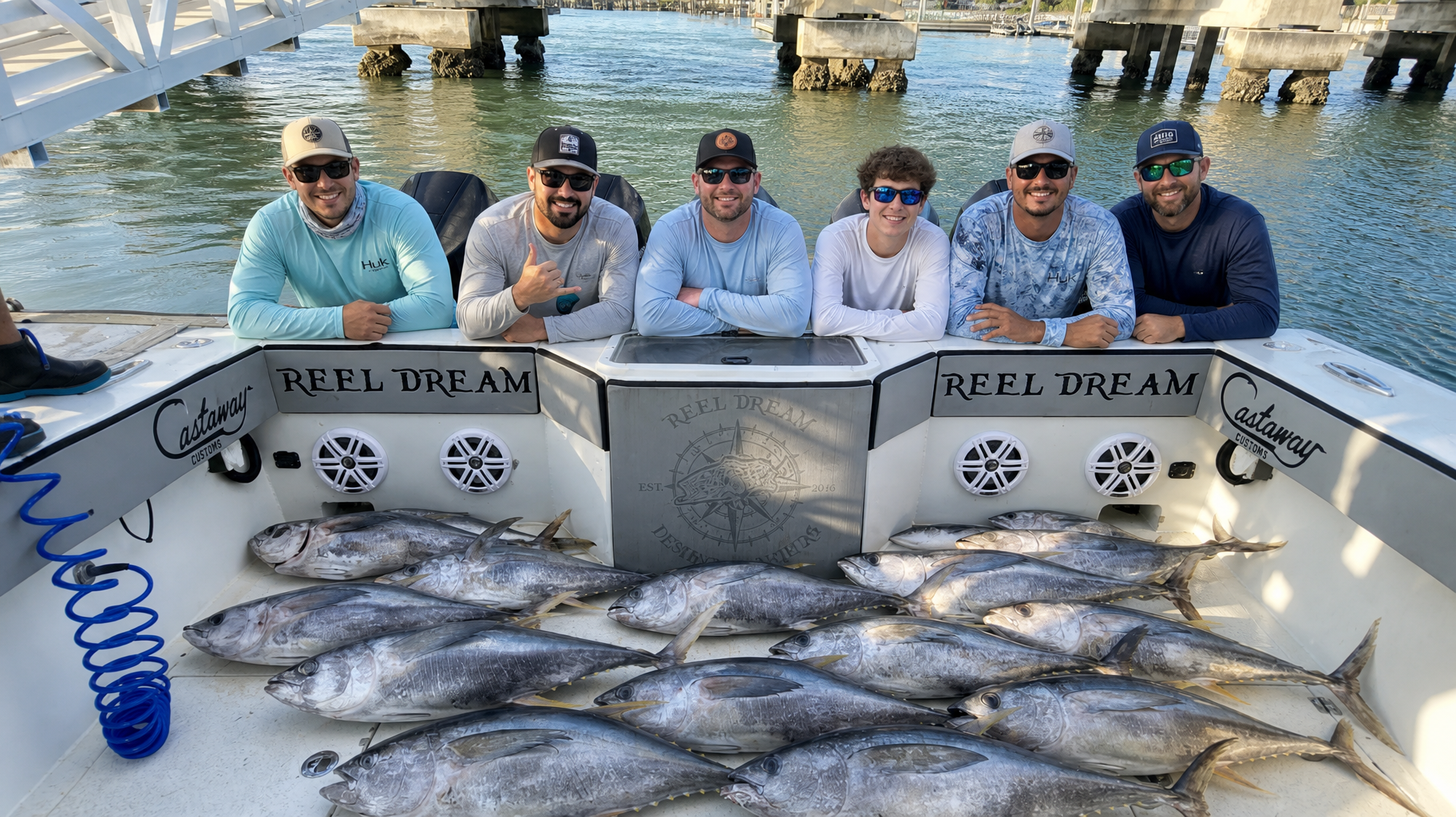 Six anglers posing on a boat deck with a large pile of caught fish at their feet.