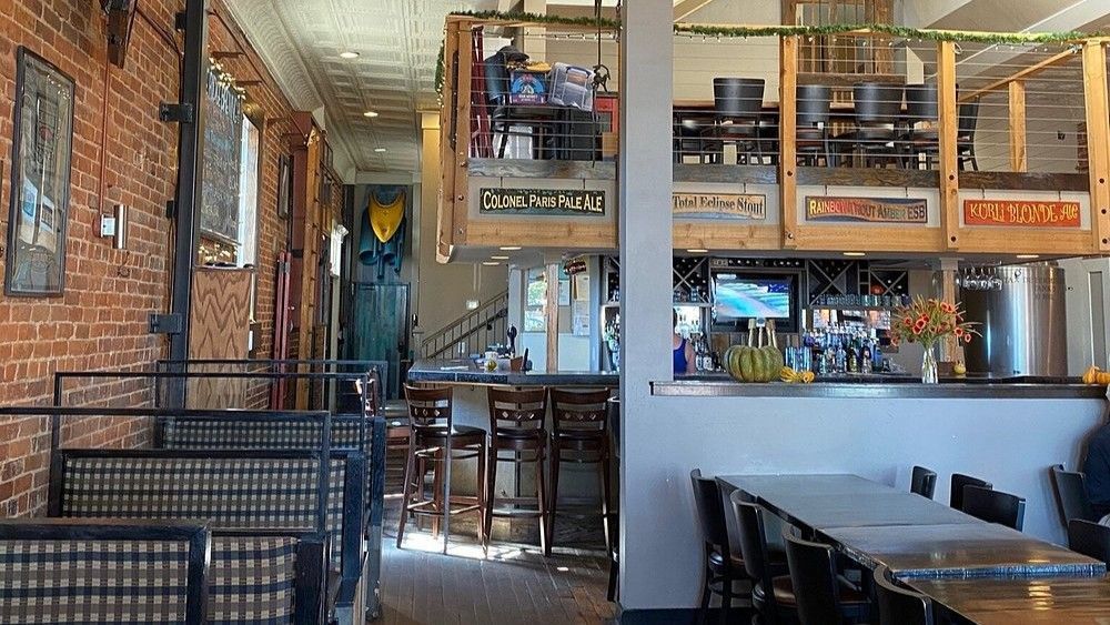 The interior of a restaurant with brick walls, booth seating, a bar area, and an elevated seating loft.