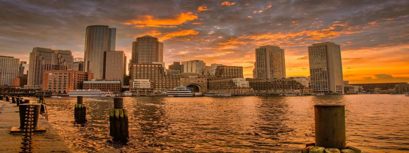Boston leads Massachusetts in short-term rental regulation and enforcement Boston skyline at sunset viewed from the harbor—an iconic Massachusetts destination with strict STR rules