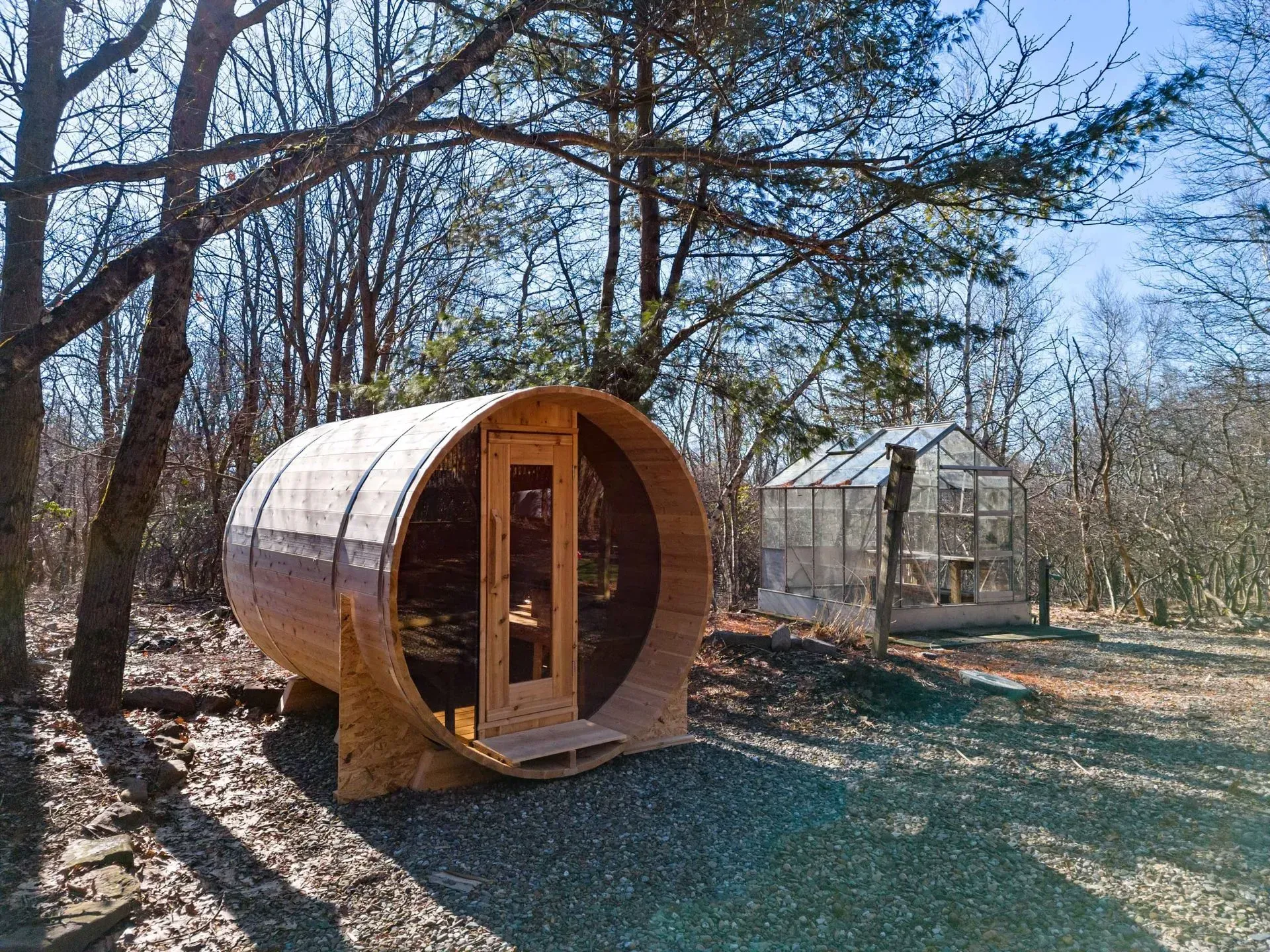 A wooden barrel is sitting in the middle of a forest next to a greenhouse.