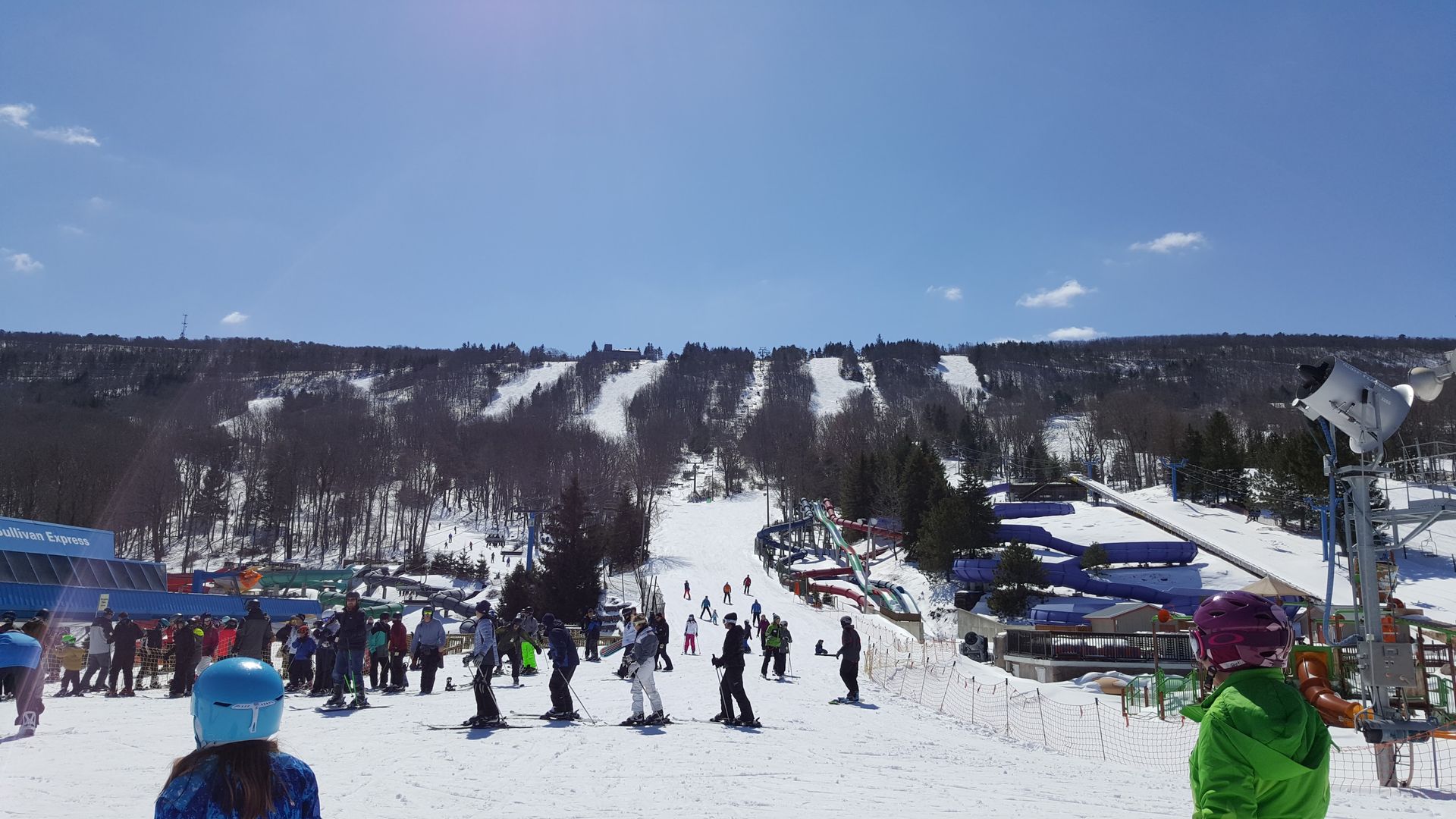 Skiers and snowboarders on a snow-covered mountain slope, with a clear blue sky.
