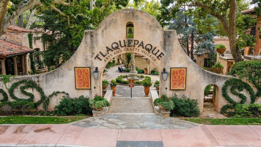 The arched stone entrance of Tlaquepaque Arts and Crafts Village in Sedona, surrounded by greenery and trees.