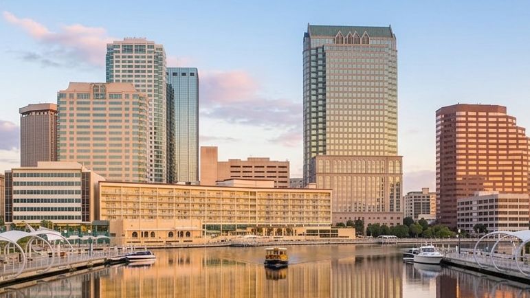 City skyline with high-rise buildings reflected in a calm waterfront at sunset