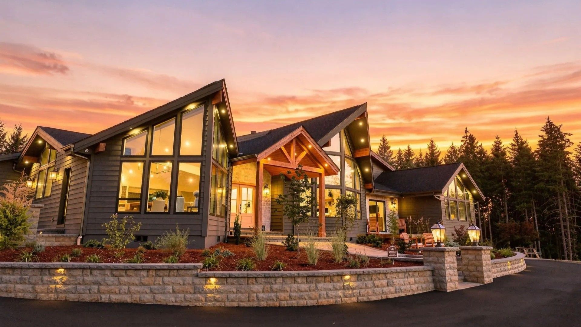 Modern mountain lodge at sunset with warm glowing windows and stone landscaping