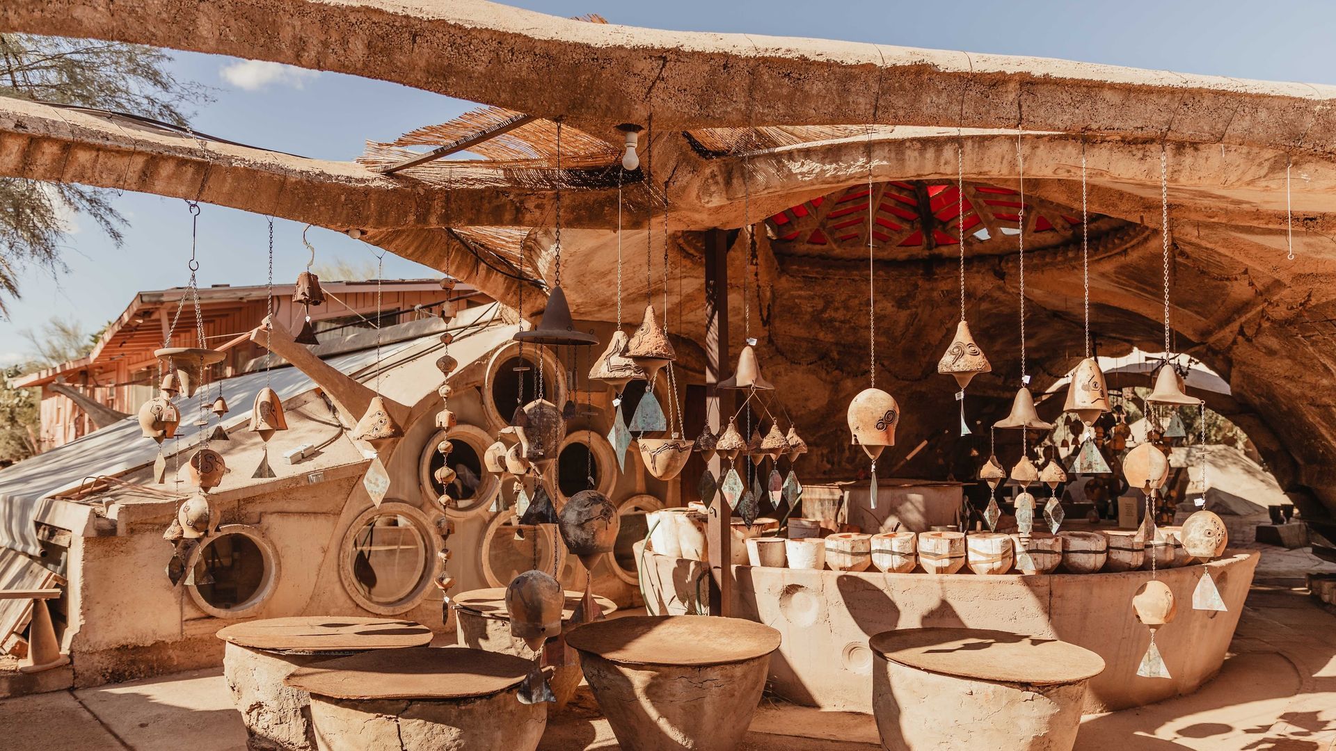 Artistic outdoor market with handmade goods under a curved, earthen roof.