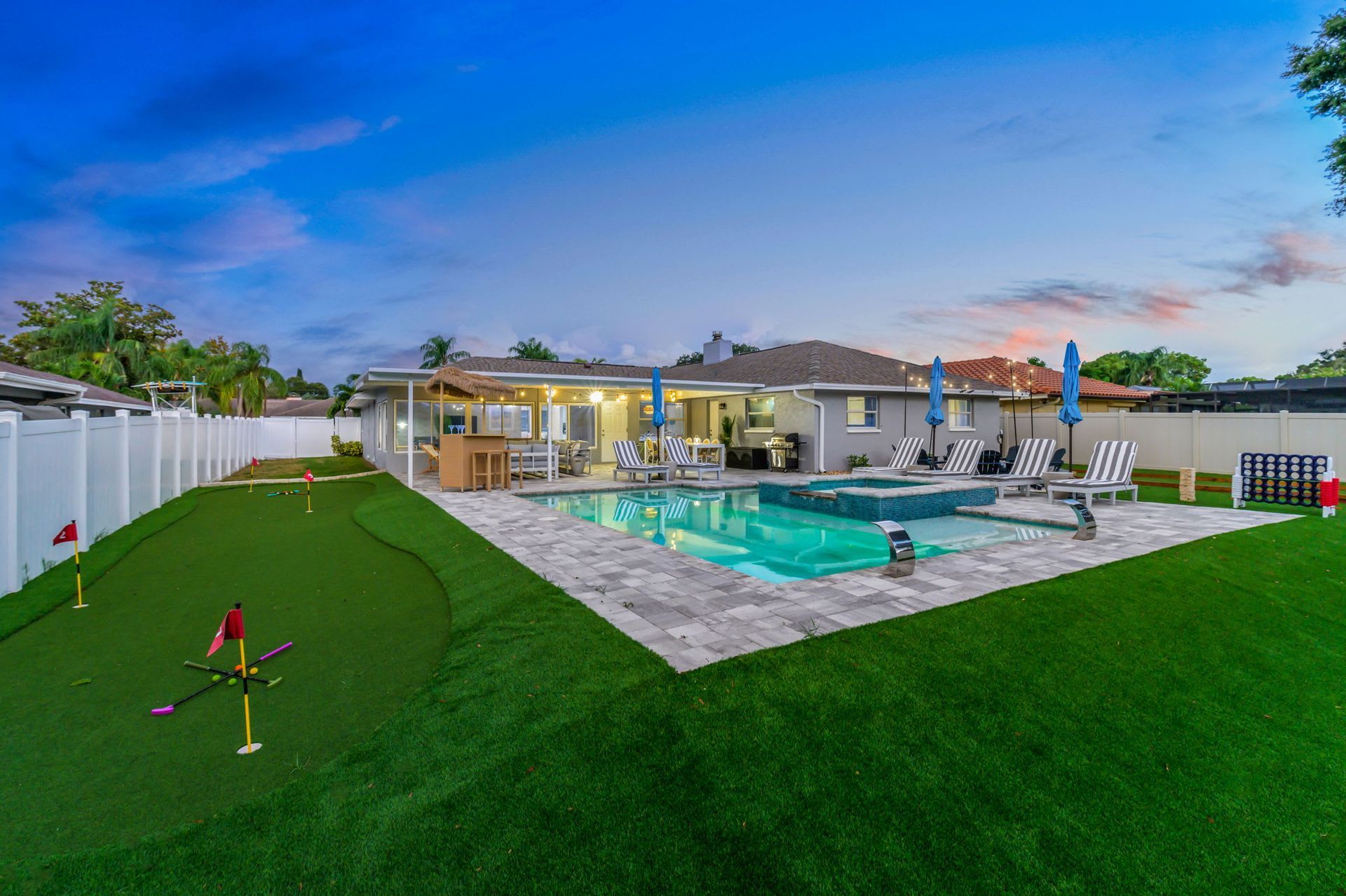 Backyard patio with swimming pool, lounge chairs, and green lawn at dusk