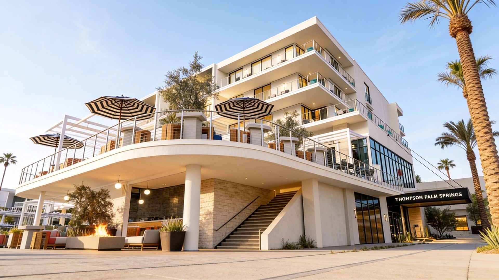 Modern multi-story resort hotel with white balconies and palm trees at sunset