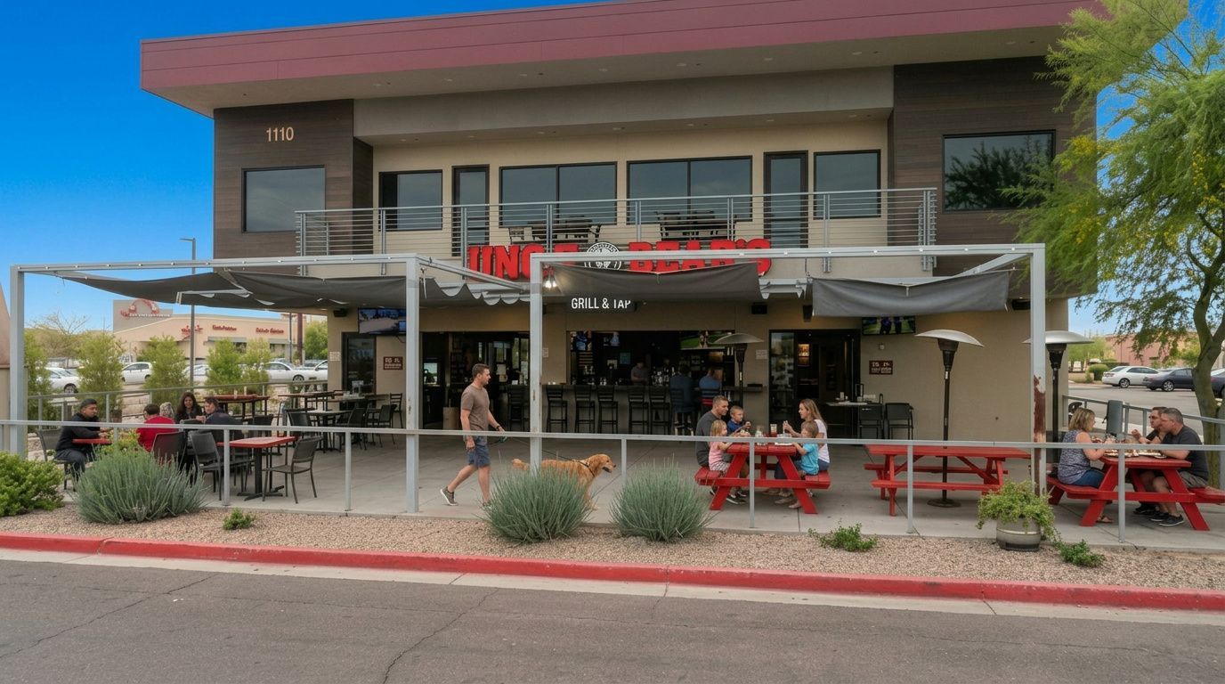 Outdoor café patio with red tables and umbrellas outside a two-story building under a clear blue sky