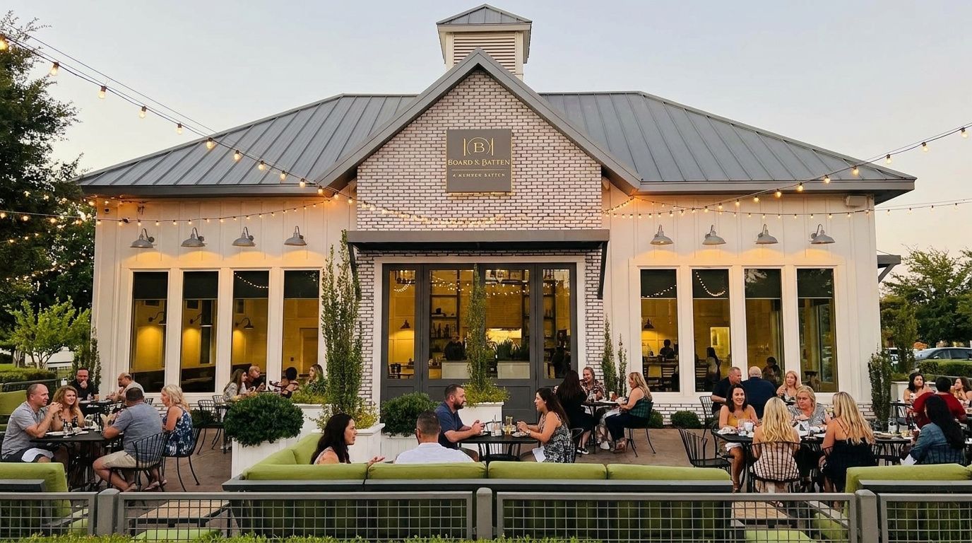 Outdoor patio dining at a white brick restaurant with a metal roof and warm evening lights