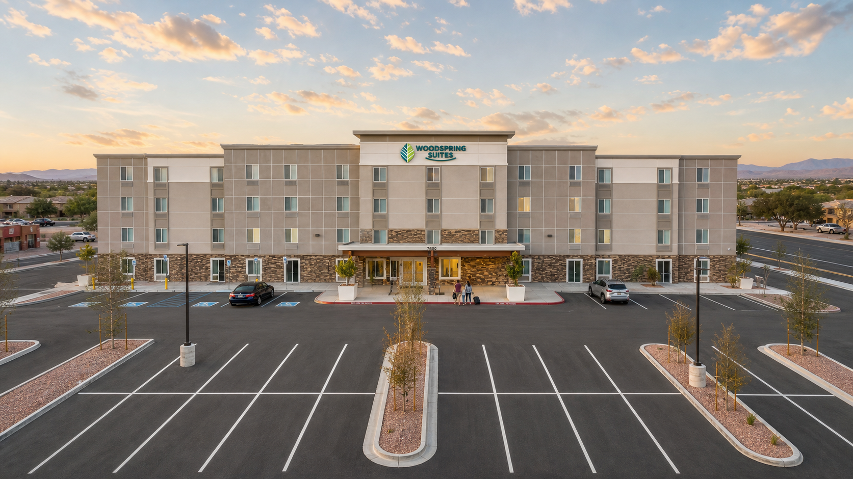 Modern four-story hotel with parking lot at sunset, front entrance centered under a clear sky