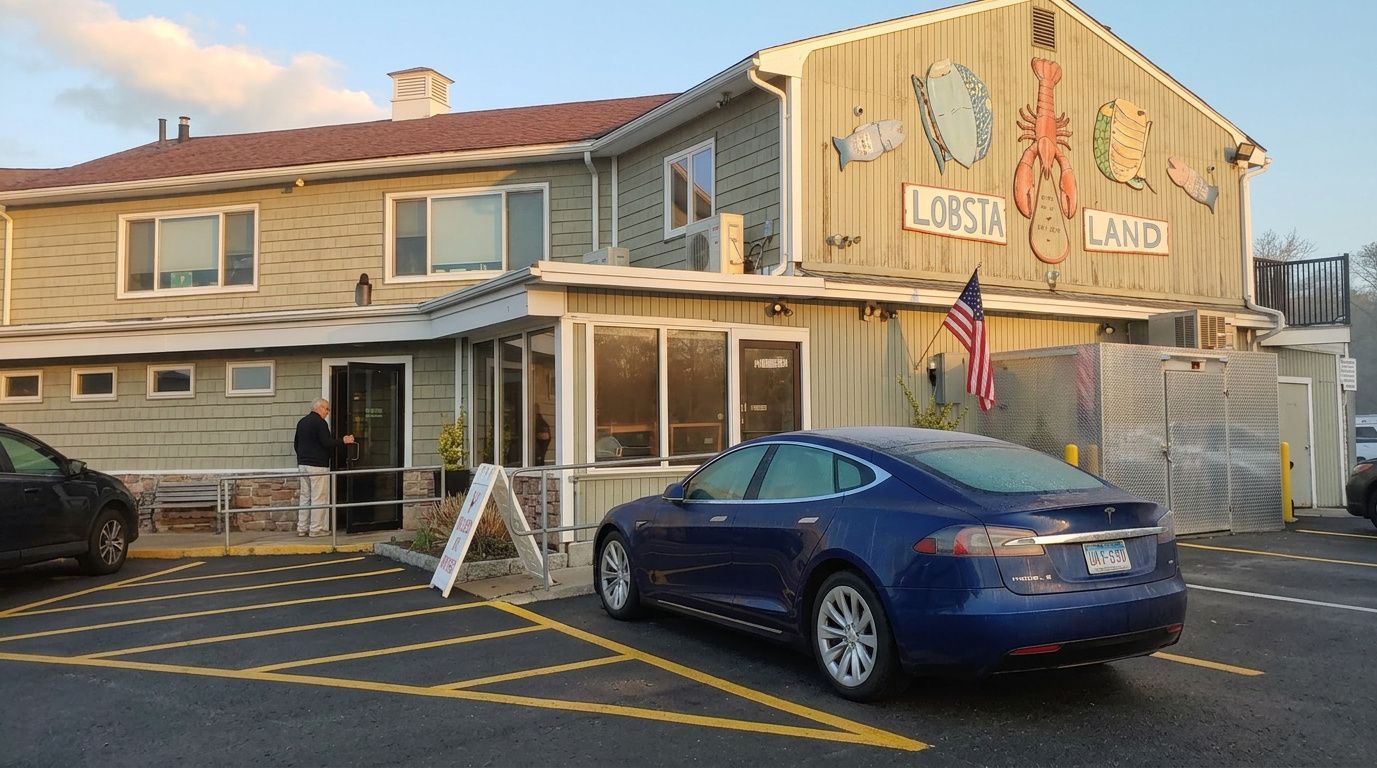 Two-story tan building with a blue car parked in front and a colorful sign by the entrance