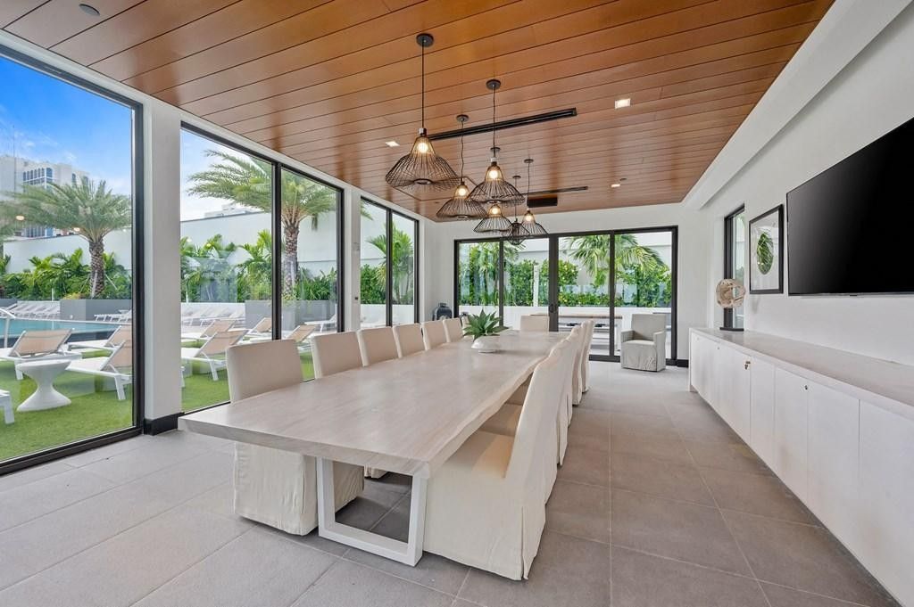 Modern dining room with long table, white chairs, wood ceiling, and large glass doors opening to a patio.