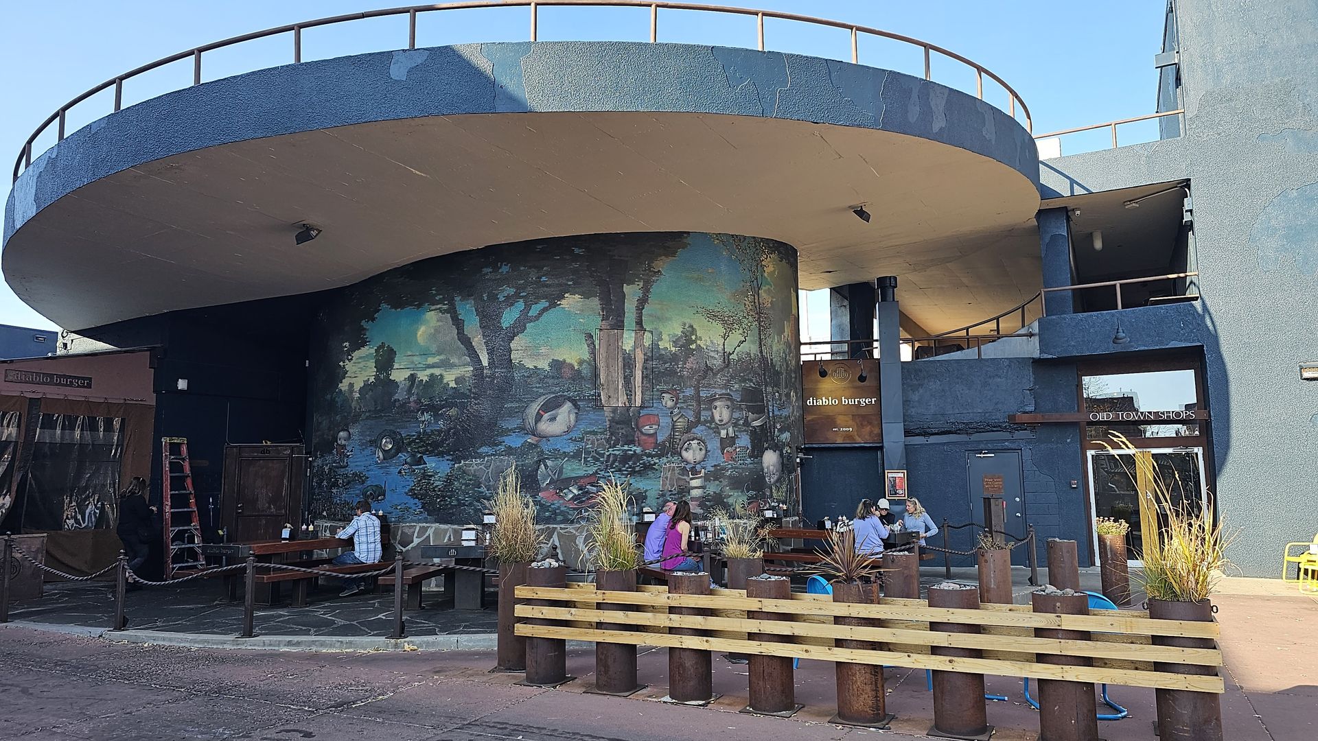 Restaurant exterior with mural, outdoor seating, and blue tile facade.