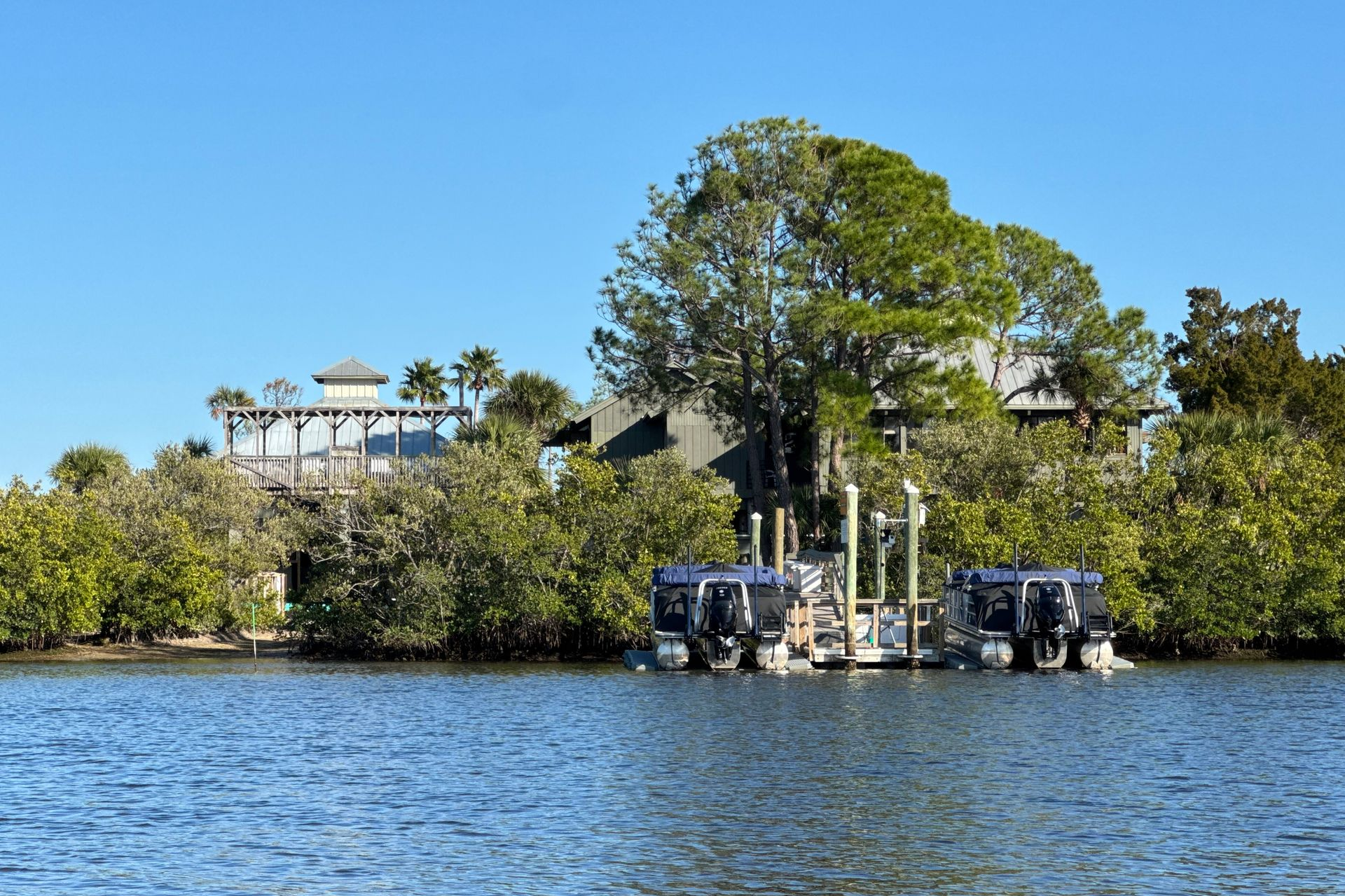 Boats docked at a pier, with buildings and trees in the background under a clear, blue sky.