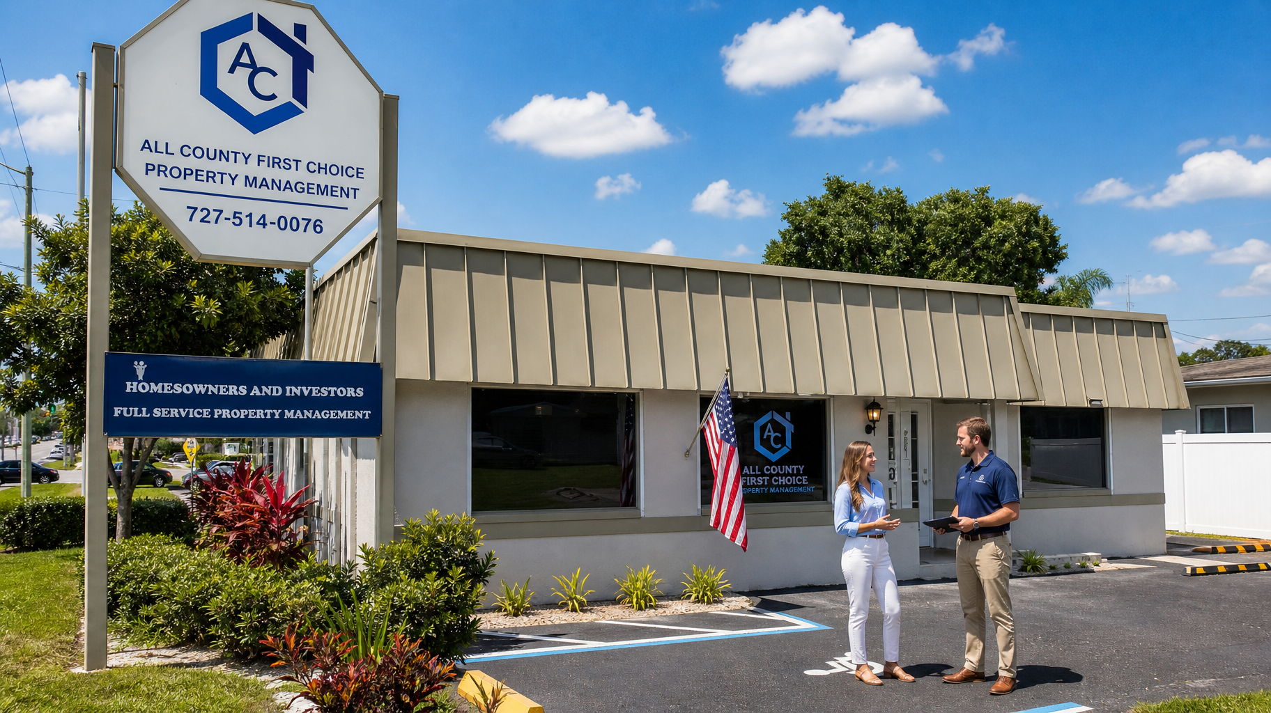 Two people stand outside a beige building with a sign and American flag on a sunny day.