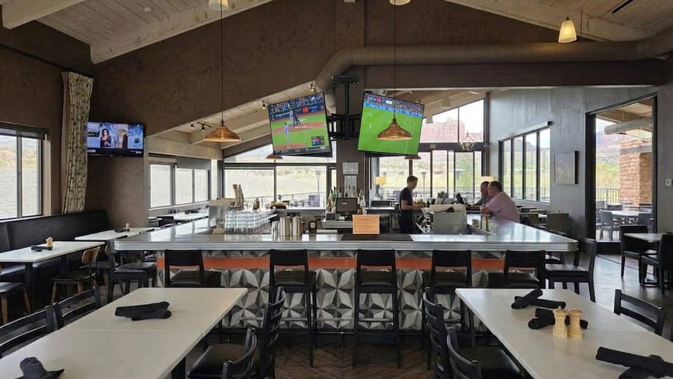 A spacious, modern restaurant bar with white tables, black seating, and multiple televisions playing sports.