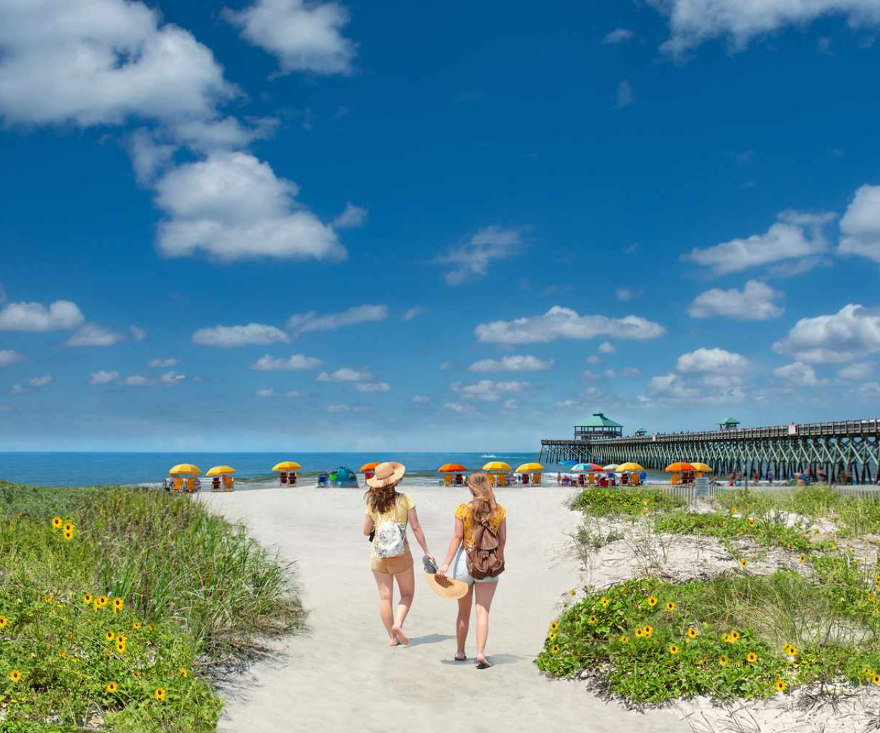 Two women are walking down a path to Folly Beach in South Carolina