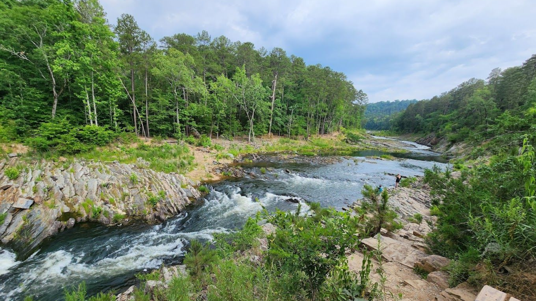 River flowing through a rocky gorge surrounded by green trees under a cloudy sky.