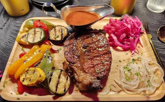 Grilled steak with vegetables, sauce, and pickled cabbage on a wooden platter.