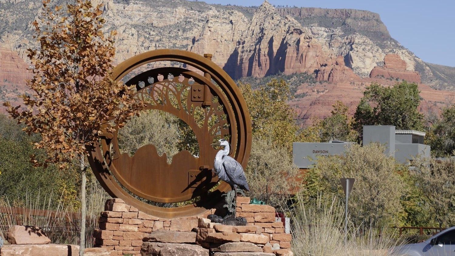 Sculpture of a heron in front of a rusty metal circle, Sedona red rock mountains in the background.