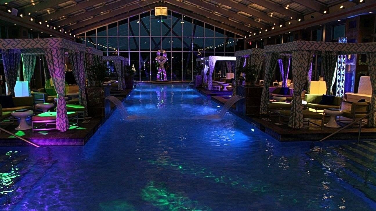 Indoor swimming pool with cabanas, lit by blue and purple lights.