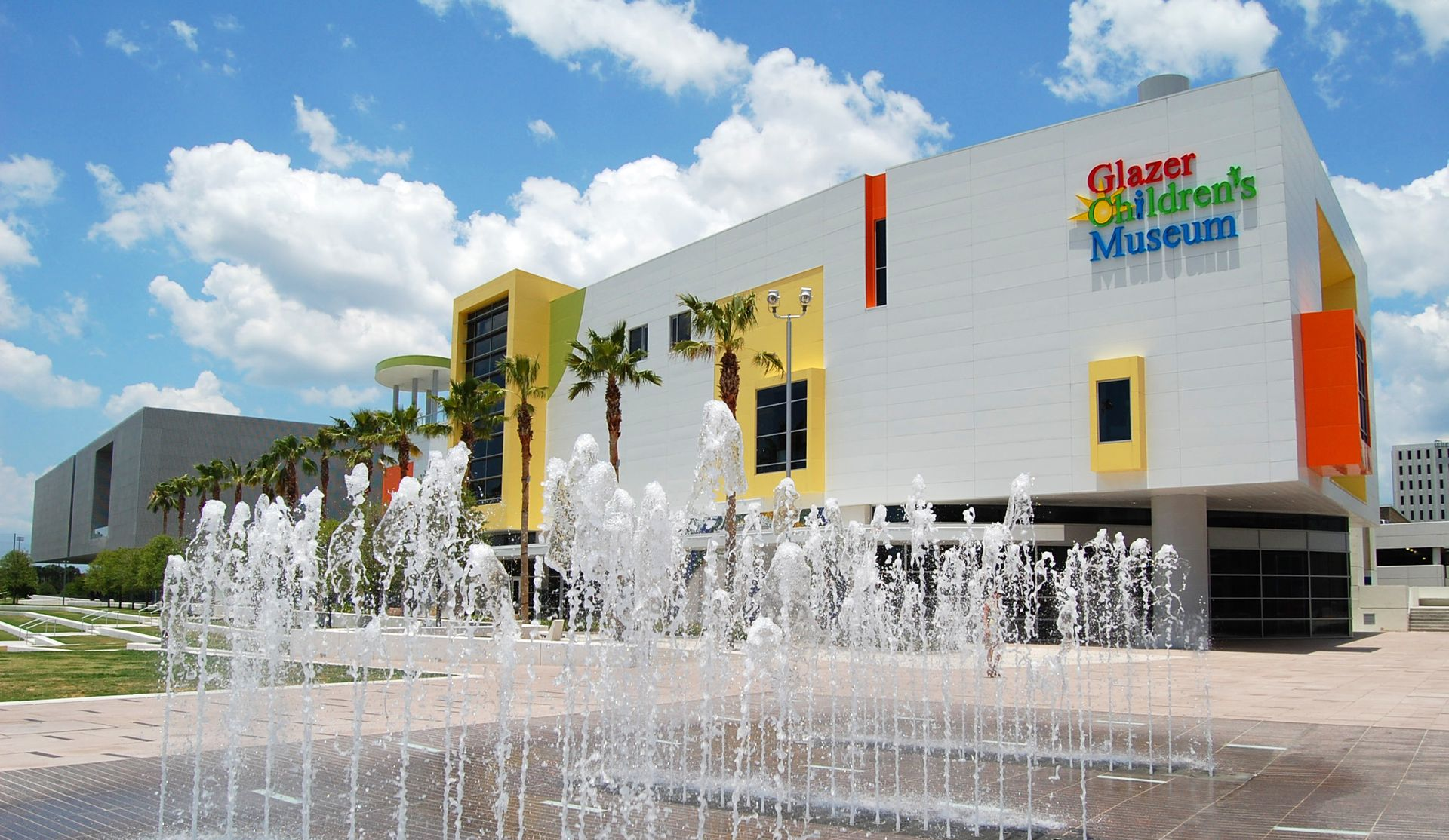 Glazer Children's Museum building exterior, bright colors, water fountain in foreground, blue sky, palm trees.