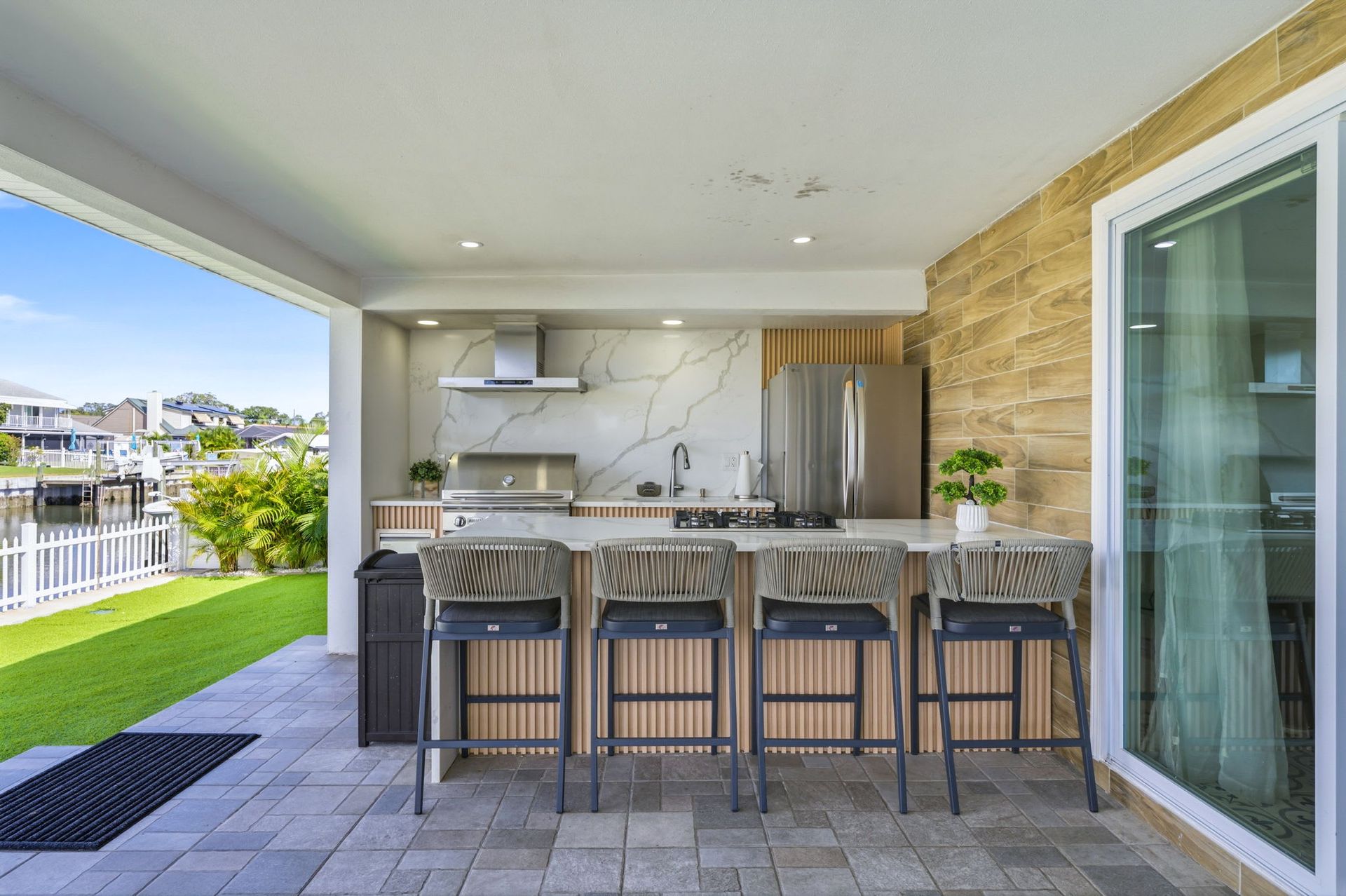 Outdoor kitchen with bar seating, stainless steel appliances, and canal view.