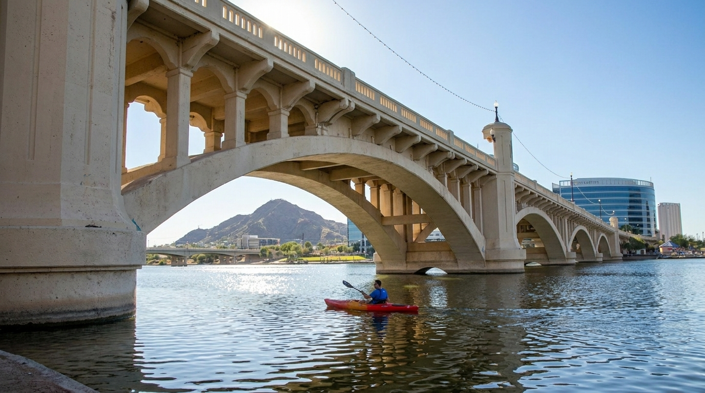 Red arched bridge over water with a lone kayaker beneath it on a sunny day