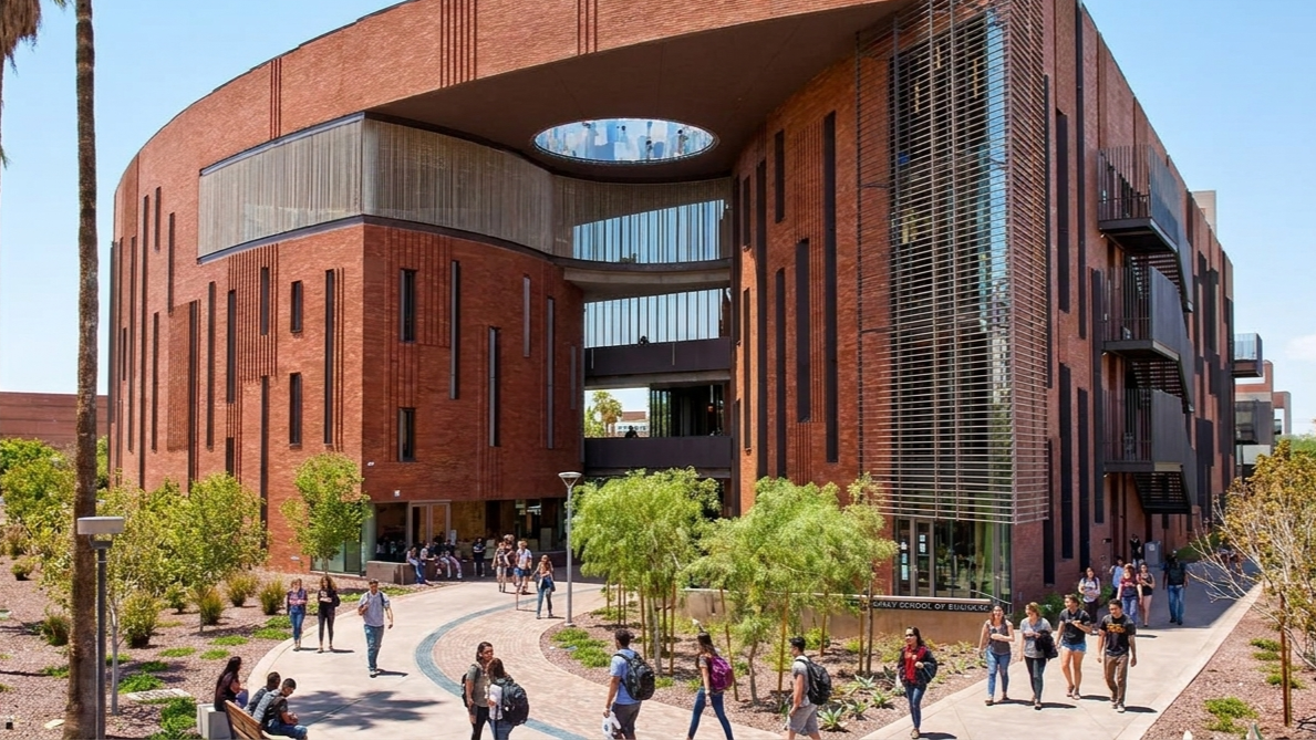 Modern red-brick circular building with a large opening, glass facade, palm trees, and people walking outside