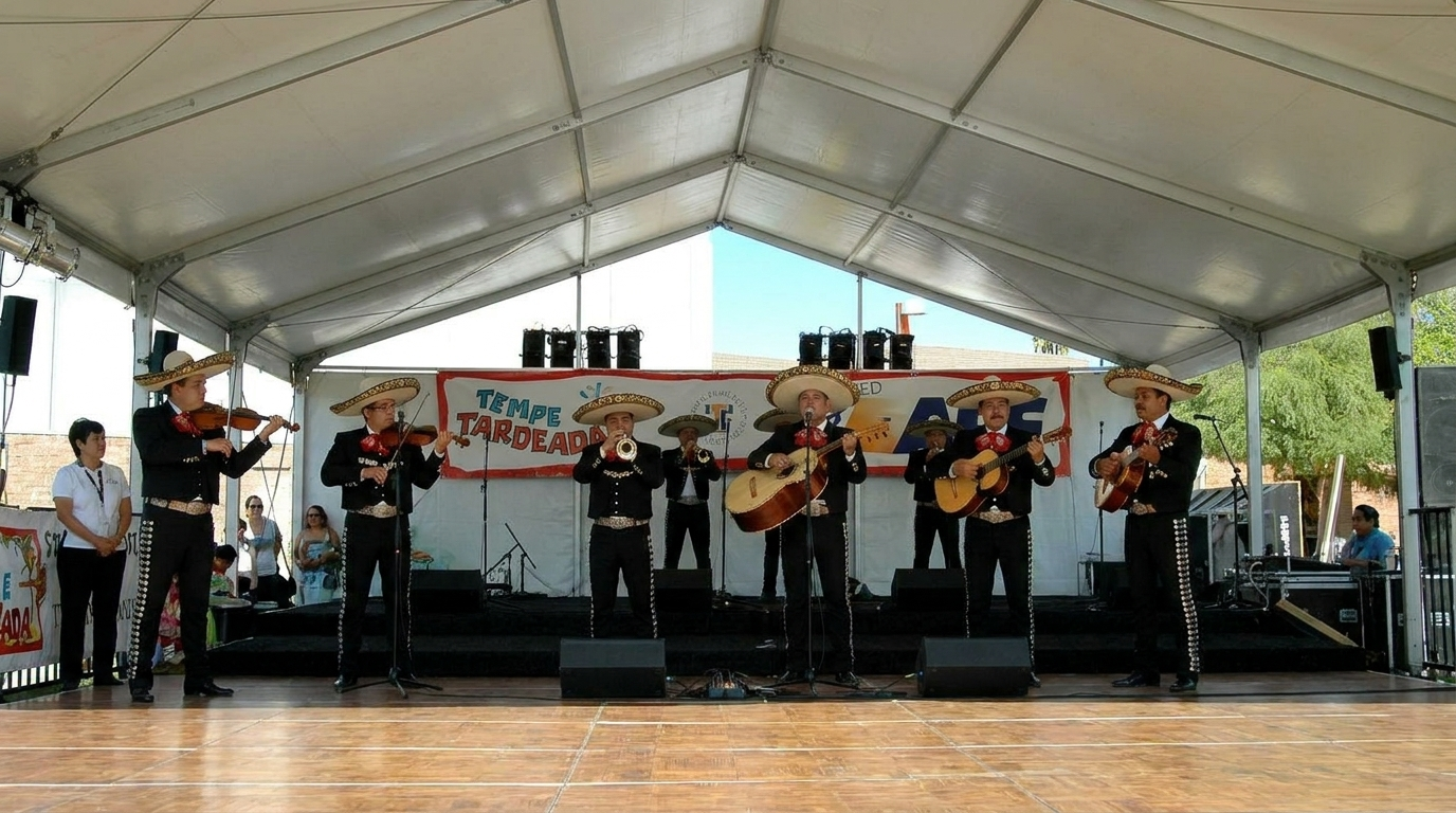 Mariachi band performing on an outdoor stage under a white tent, with guitars and violins.