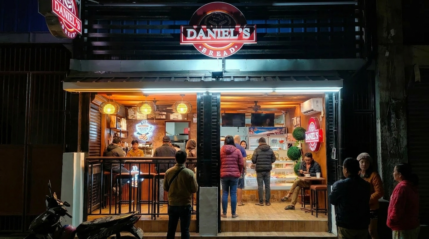 Nighttime storefront with warm lights, people browsing inside and standing outside.