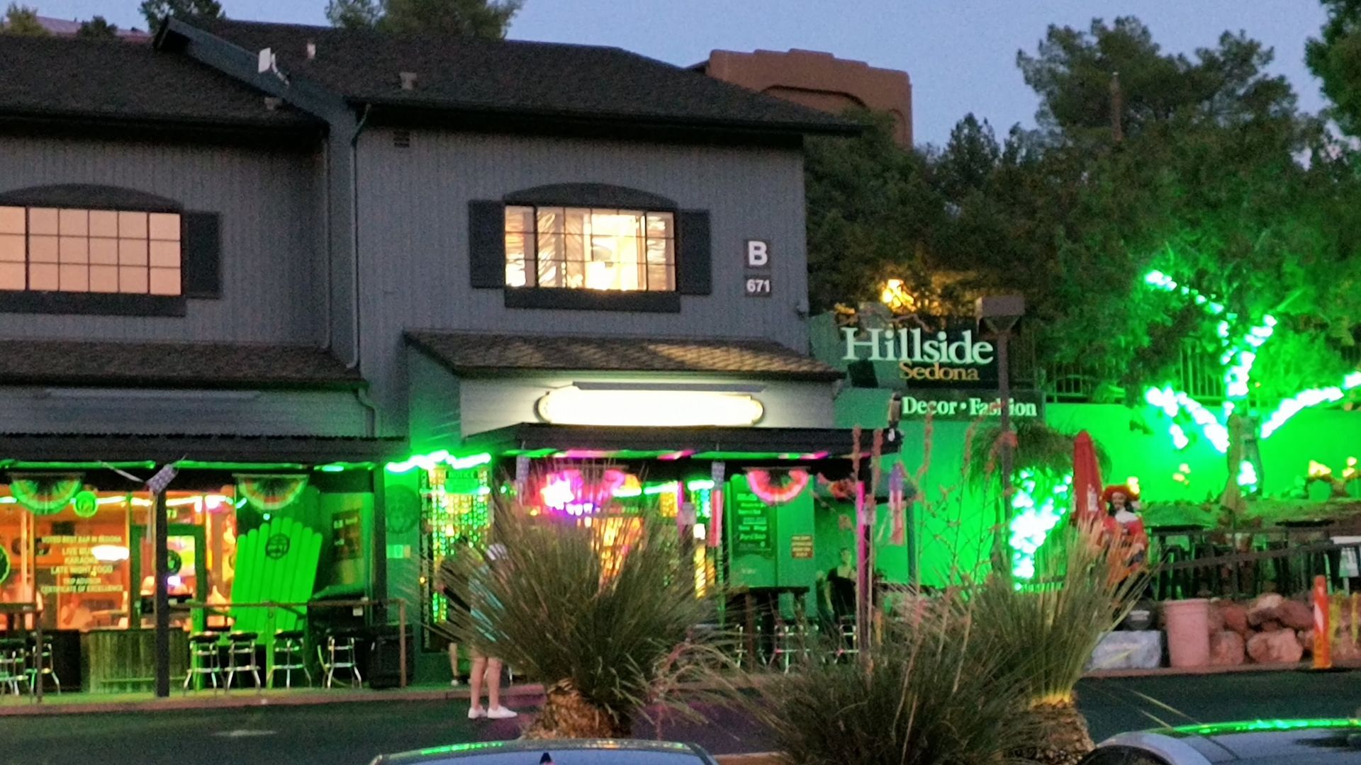 Hillside Tavern bar exterior, lit green, with illuminated sign and plants.
