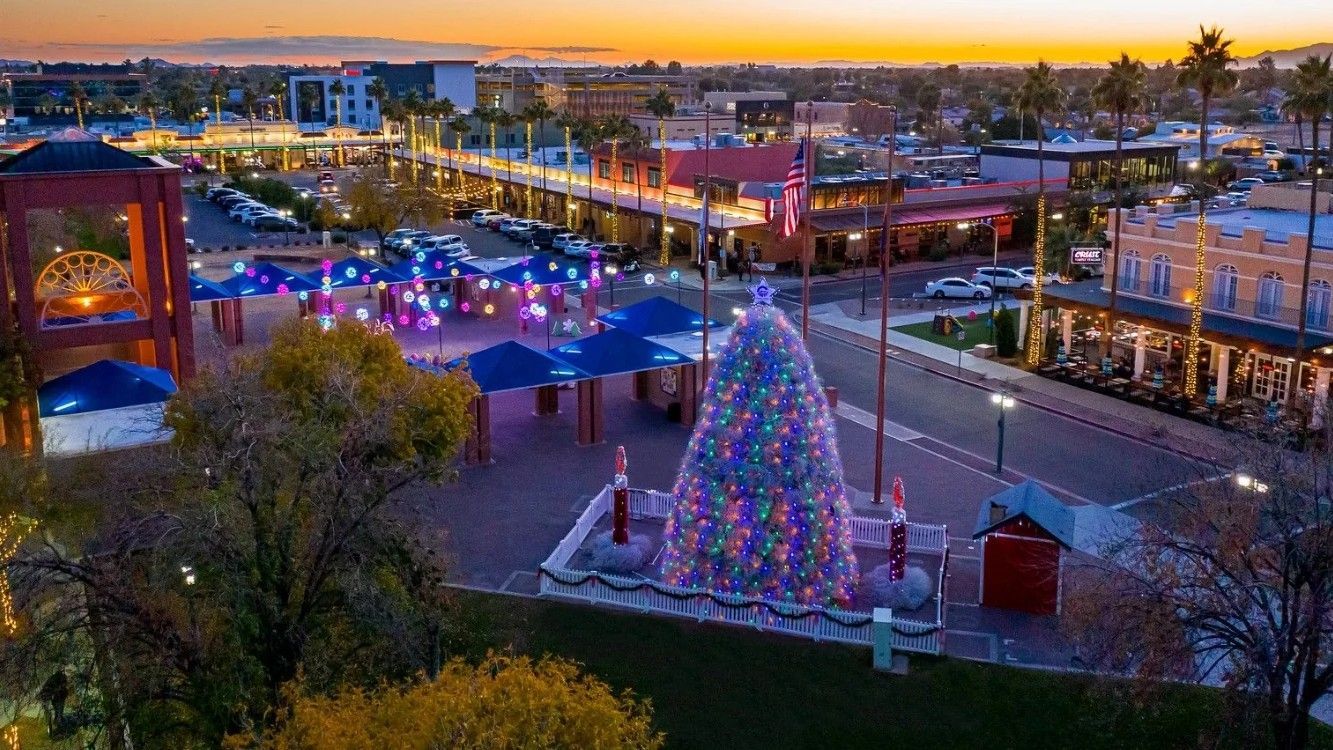 Town square at dusk, Christmas tree lit with colorful lights, buildings, street lights.