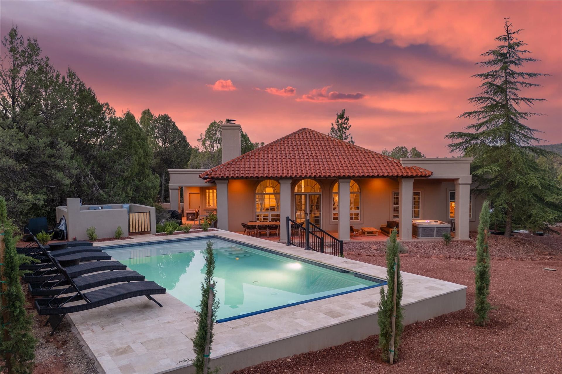 A desert home with a terracotta tile roof and pool sits under a vibrant pink and purple sunset.