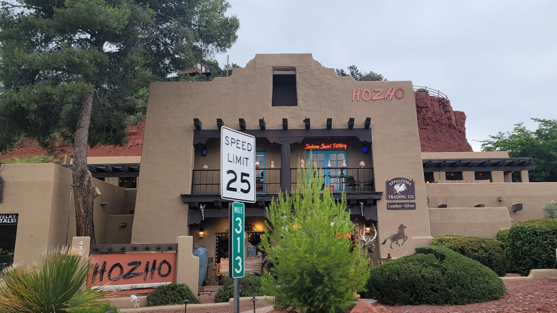 Hozho restaurant exterior, brown adobe style building with speed limit sign, bushes, and a horse graphic.