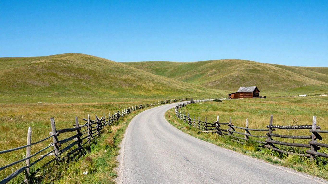 Winding country road through green hills past a small red barn under a clear blue sky