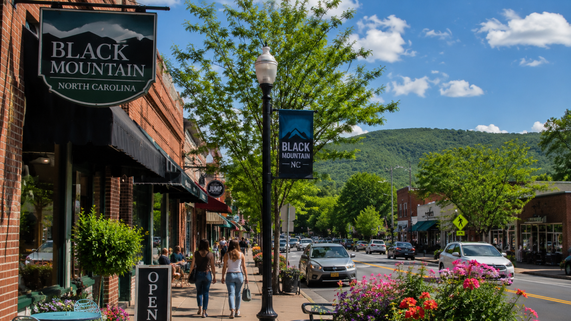 Small-town main street with shops, pedestrians, flowers, and a mountain backdrop under a blue sky