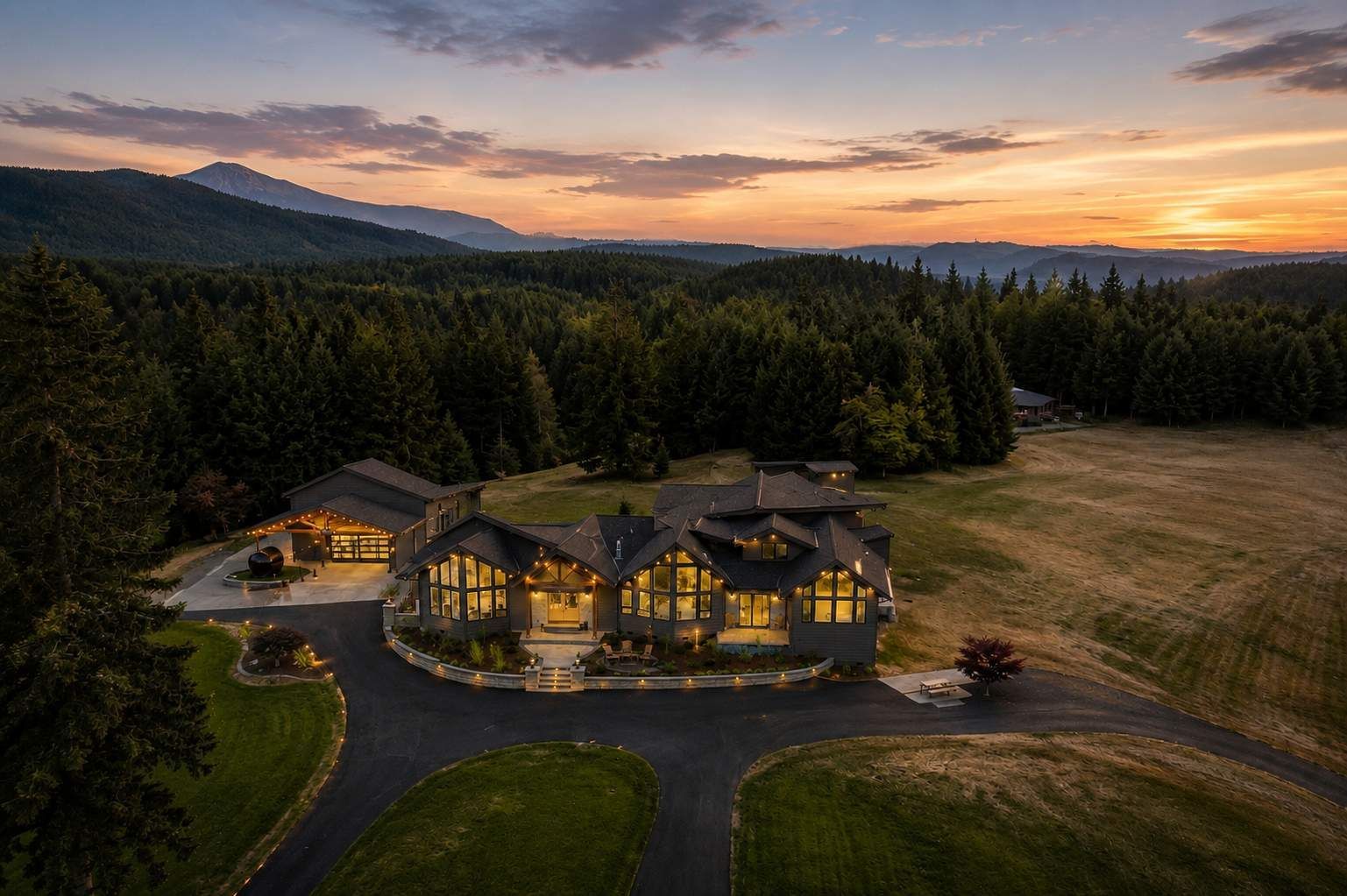 Luxury lodge at dusk with glowing windows, surrounded by forest and mountains under a colorful sunset.